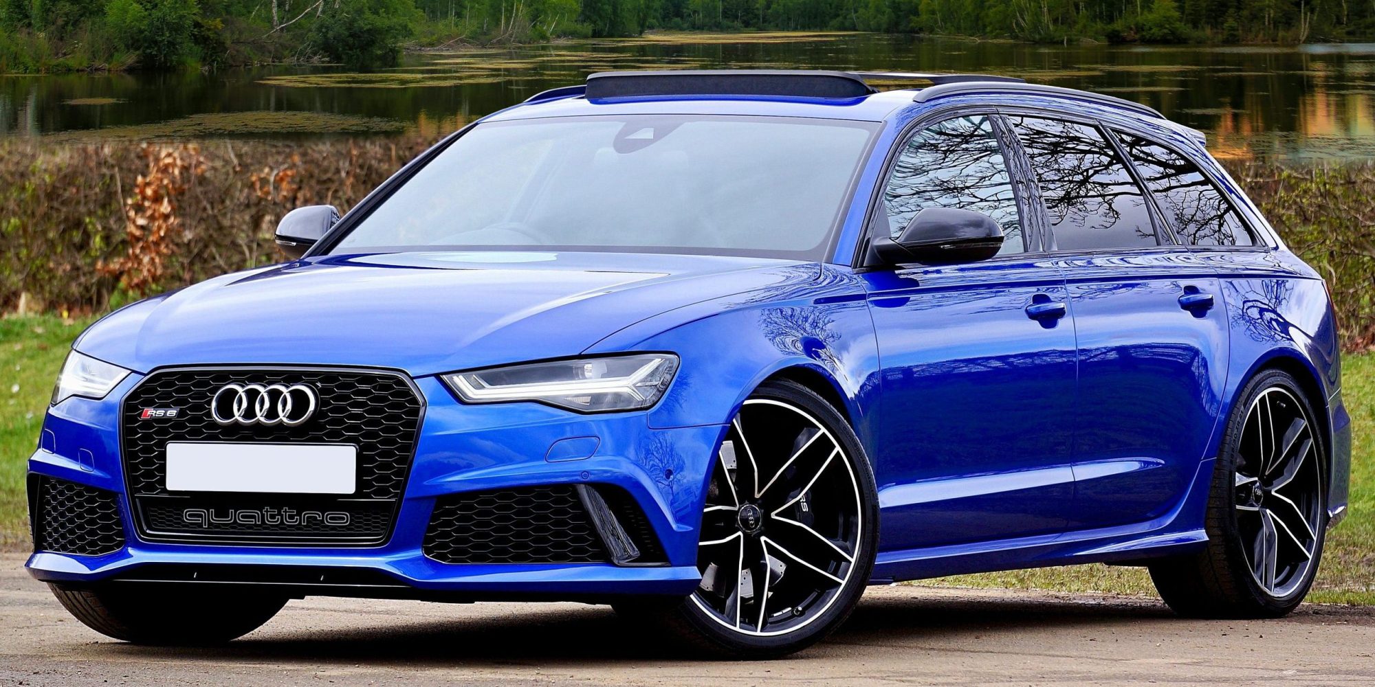 A modern blue Audi RS6 parked by a lake with scenic forest and sky backdrop. | Audi wheel spacers & adapters