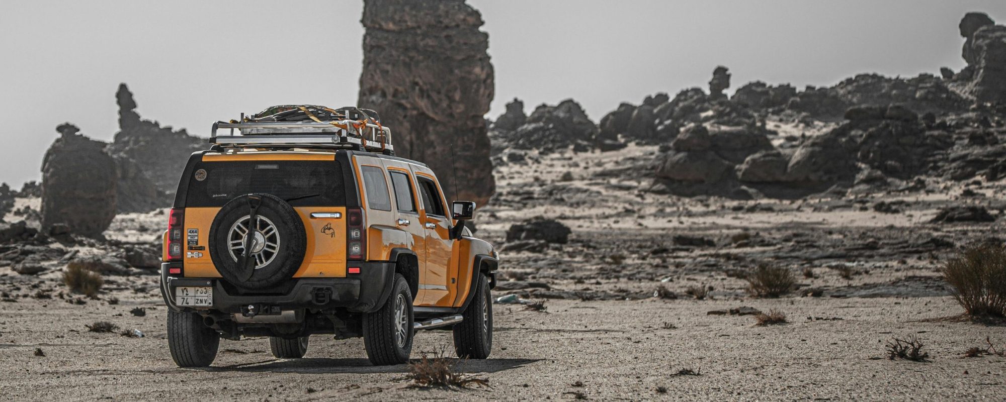 Yellow SUV exploring rugged desert terrain with rocky formations.