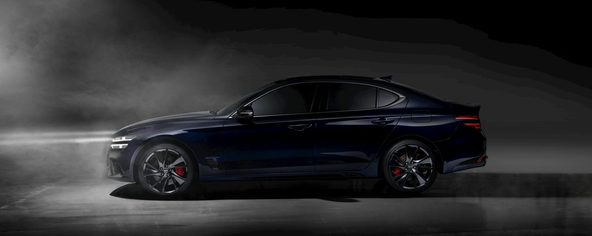 Luxury sedan with red brake calipers under dramatic lighting and smoke effect, showcasing elegance.