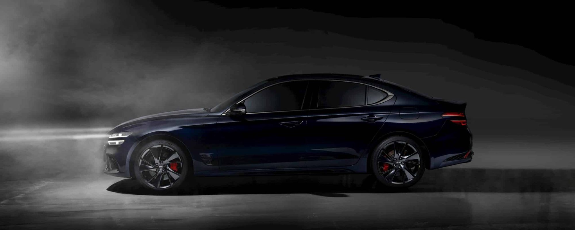 Luxury sedan with red brake calipers under dramatic lighting and smoke effect, showcasing elegance.