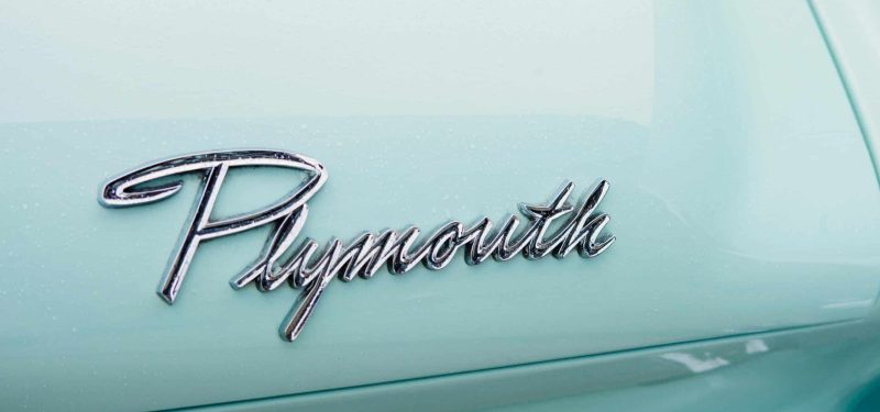 Chrome Plymouth emblem on vintage car with light blue paint and sleek design.