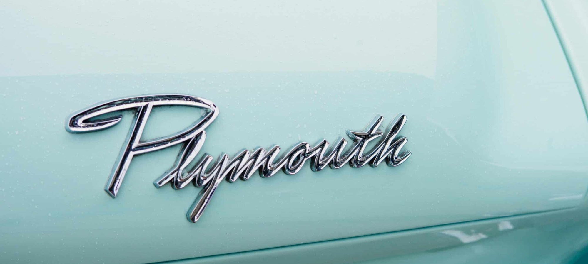 Chrome Plymouth emblem on vintage car with light blue paint and sleek design.