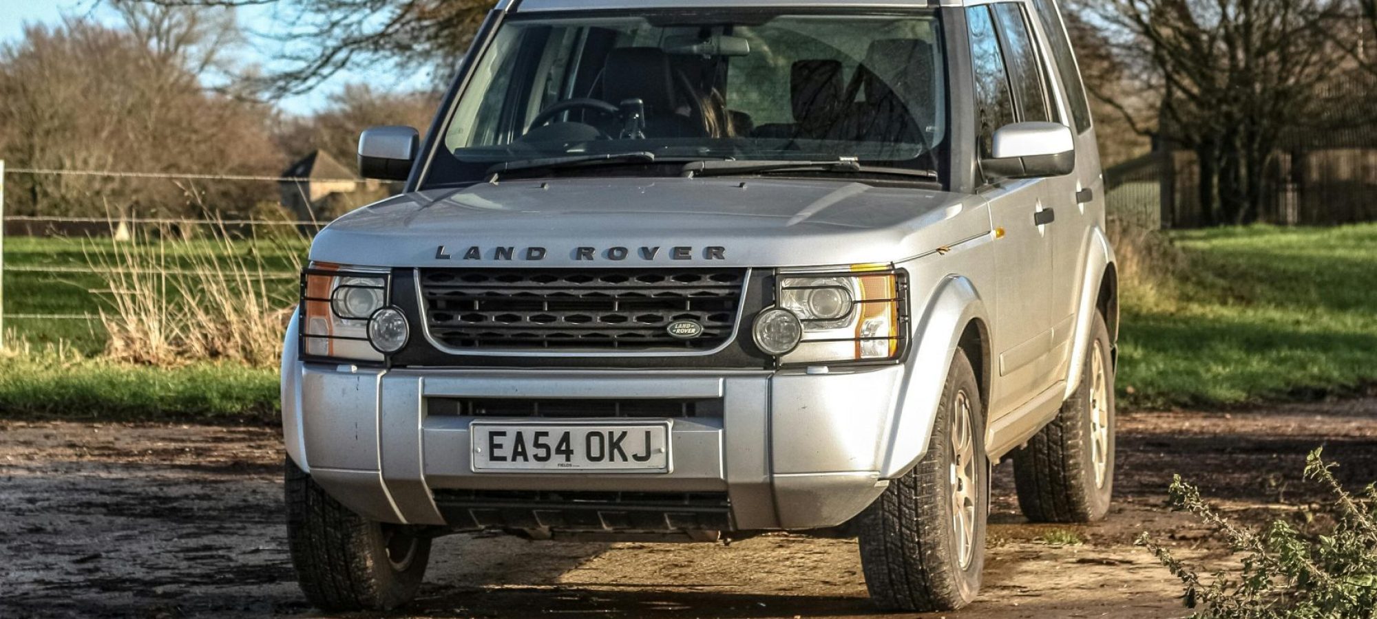 Land Rover SUV parked on a muddy rural road in autumn countryside.