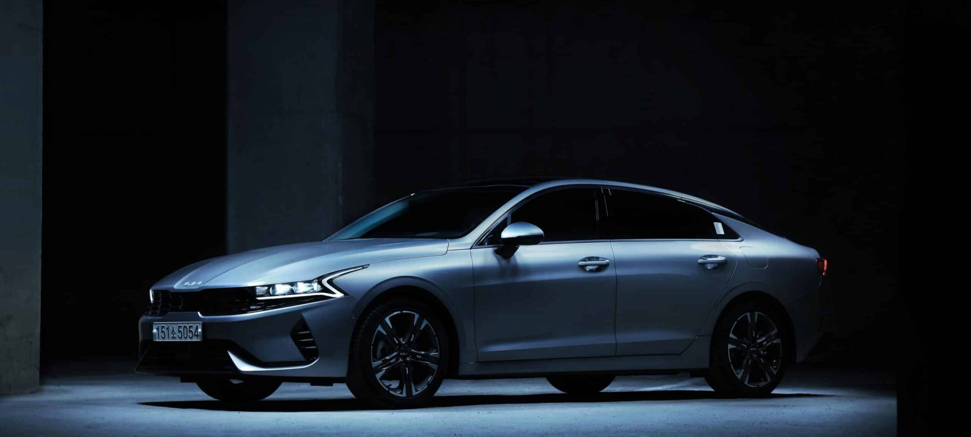 Sleek Kia K5 sedan showcased in a dimly lit indoor parking space.