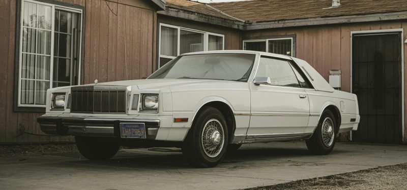 Classic white Chrysler Cordoba parked in front of a retro house with vintage style.