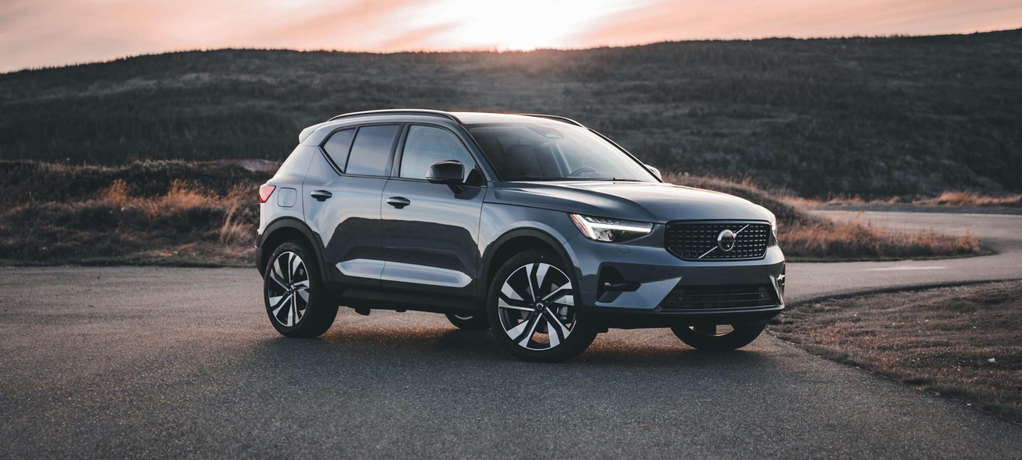A Volvo SUV parked on a scenic road at sunrise, surrounded by hills. by Erik Mclean via pexels