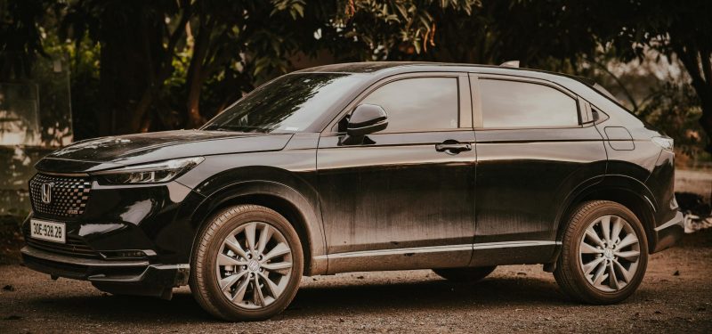 A stylish black Honda HR-V SUV parked outdoors amongst trees on a sunny day.