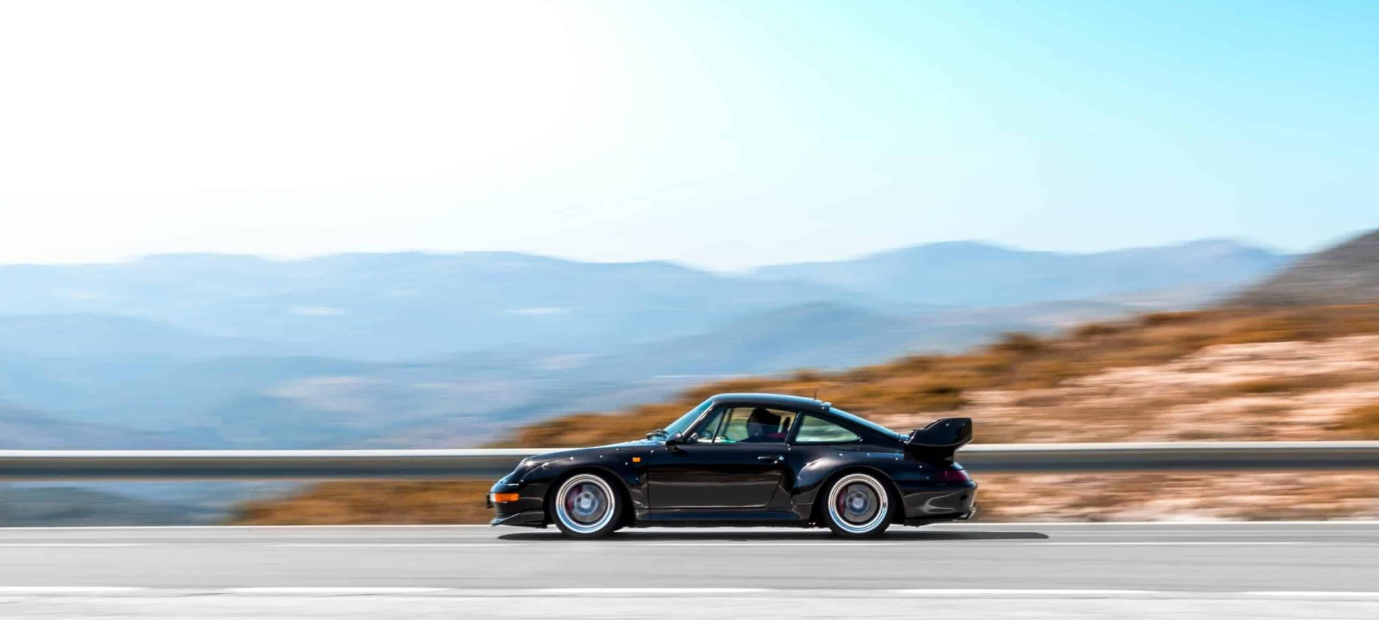A sleek black supercar speeding on a curvy mountain road during bright daytime. by Quentin Martinez via pexels