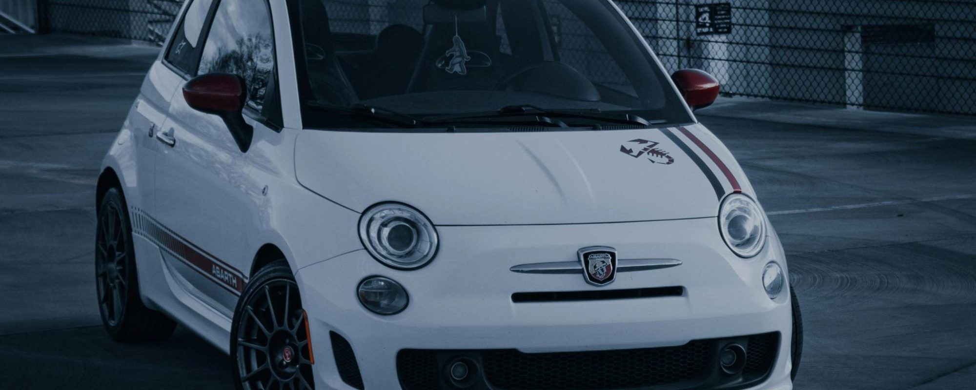 White Fiat Abarth 500 parked in an urban setting with modern architecture. by Eric Hammett Fiat Wheel Adapters / Spacers