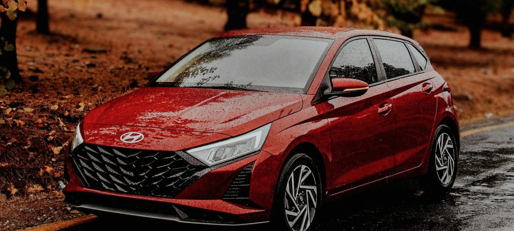 A red car hyundai on a wet road surrounded by vibrant fall foliage. Photo by Nazım can Pirinç