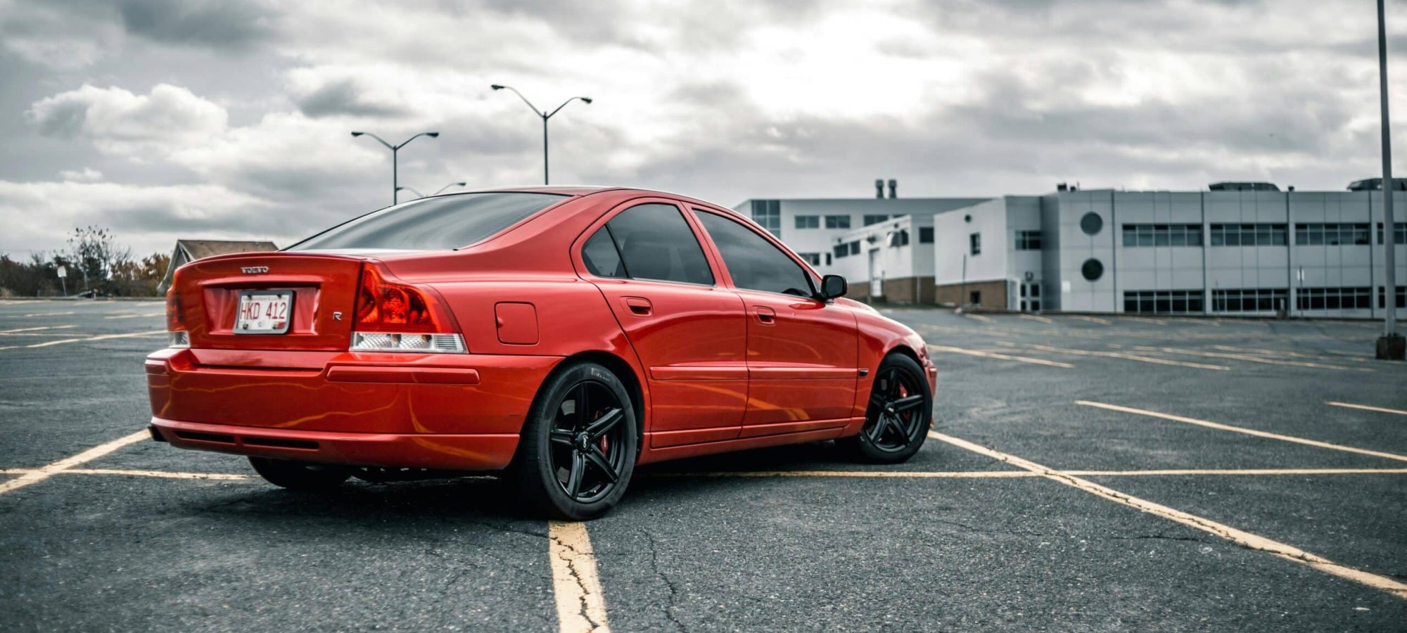 A red Volvo car parked in an empty lot under a cloudy sky, showcasing modern automotive design. by Erik Mclean via pexels