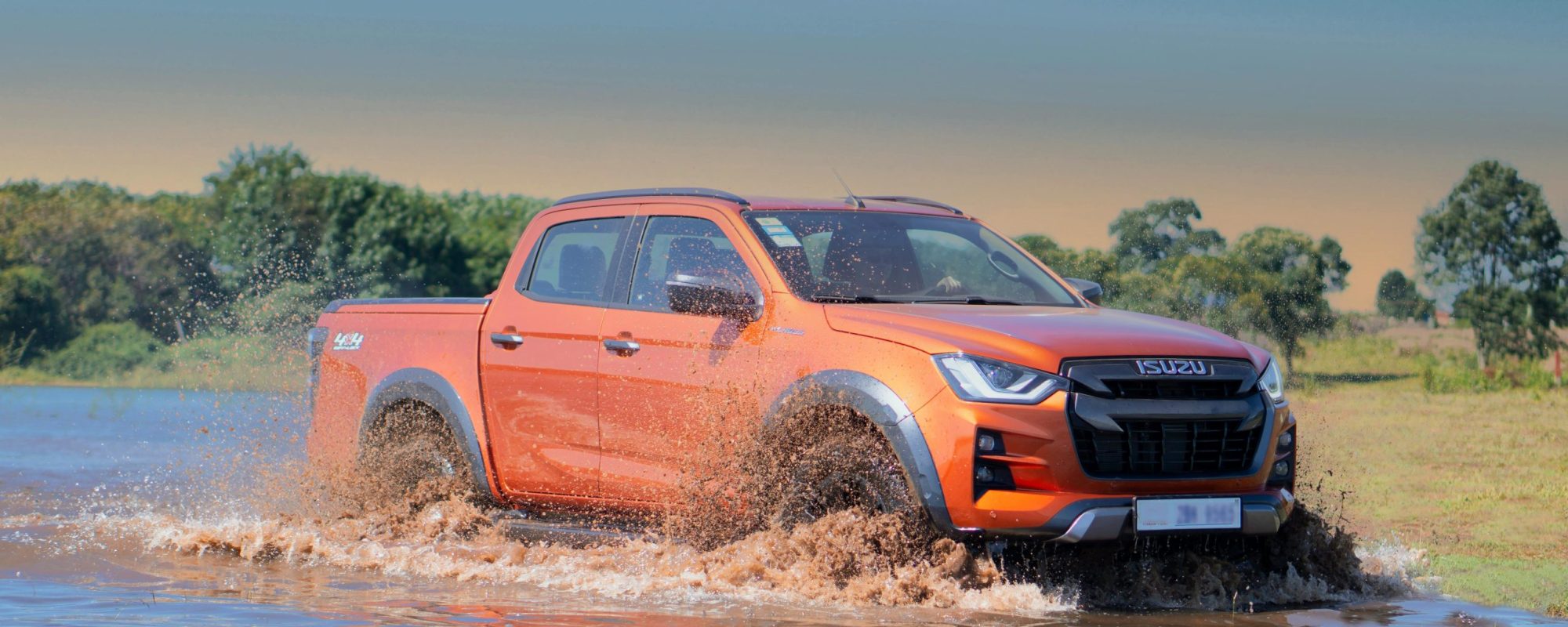An orange Isuzu D-Max pickup truck splashing through water in rugged terrain. Isuzu wheel adapters / spacers.